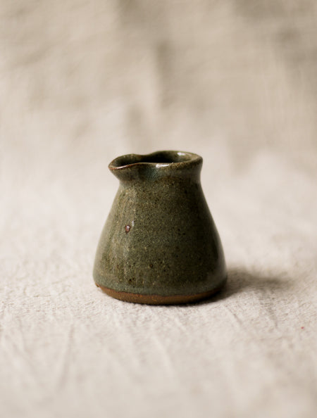 Small green ceramic milk jug on a textured beige surface