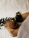 Two ceramic jugs on a wooden board with a striped fabric and greenery in the background.