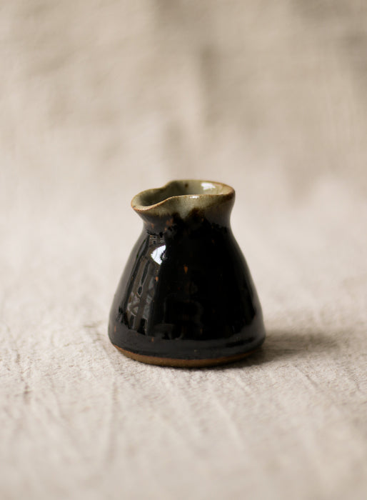 Black ceramic milk jug on a textured beige surface