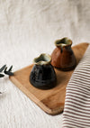 Two brown ceramic jugs on a wooden board with a striped cloth in the background