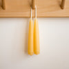 Two beeswax candles hanging on a wooden peg rack against a white wall.