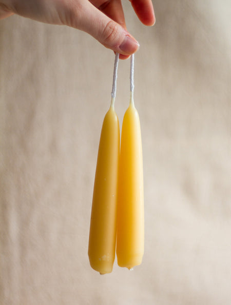 Two beeswax candles held by a hand against a beige background