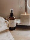 Bottle of moksa sunshine body oil on a wooden surface with a candle in the background.