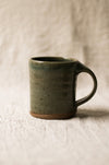 Green ceramic mug on a textured beige surface