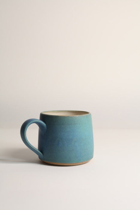 A matte turquoise stoneware coffee mug on a neutral background.