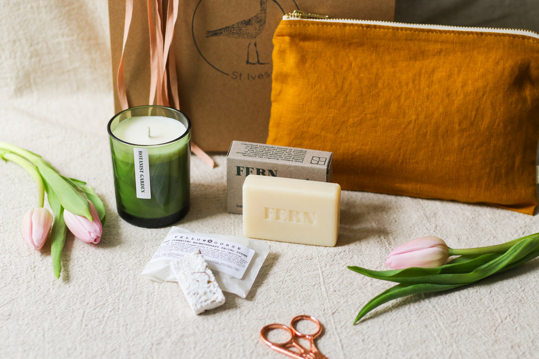 Green candle, soap, and linen pouch on a beige linen surface with tulips and sewing scissors