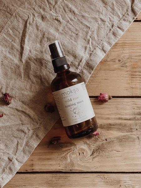 Brown glass bottle with a label on a wooden surface with linen fabric and dried flowers.