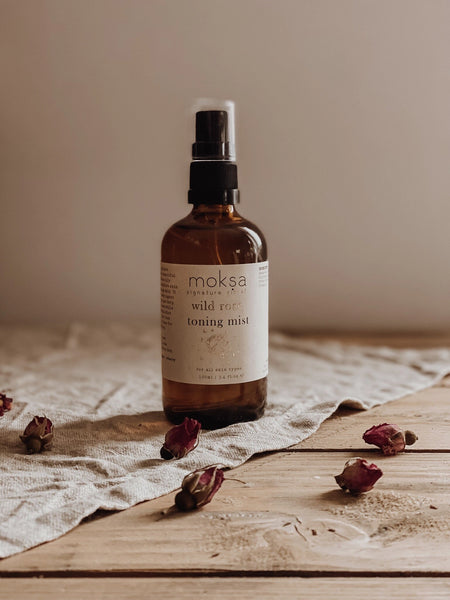 Bottle of moksa wild rose toning mist on a wooden surface with dried roses.