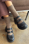 Person wearing black clogs with brown socks on a concrete floor.