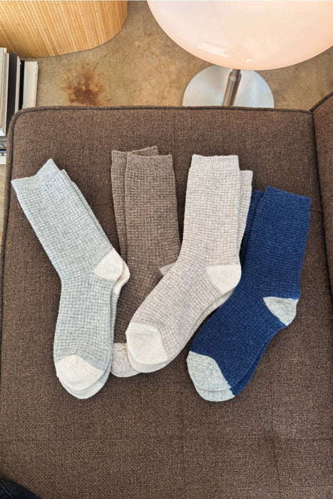 Four pairs of wool socks in grey, taupe and blue on a sofa.