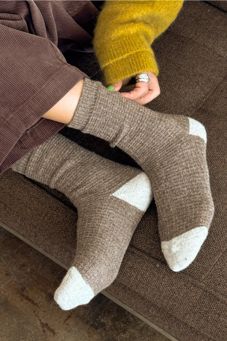 Person wearing brown wool socks , sitting on a brown sofa.
