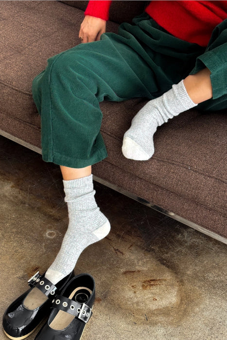 Person wearing green trousers and grey socks sitting on a brown sofa.