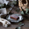 A facial clay bar on a white plate with green leaves and a woven basket in the background