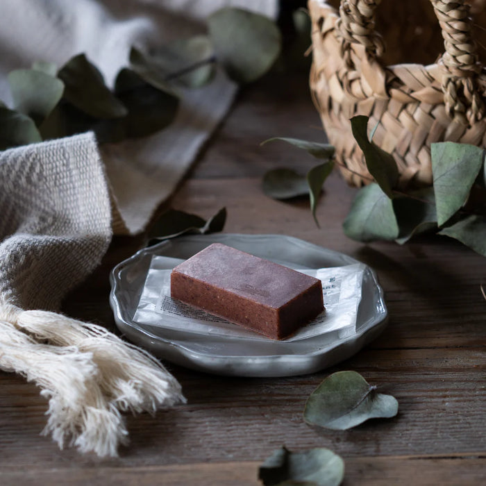 A facial clay bar on a white plate with green leaves and a woven basket in the background