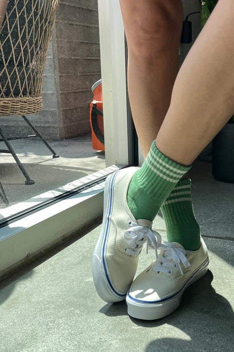 Person wearing green socks and cream trainers in and indoor setting