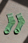 A pair of green socks with white stripes on the ankle area, displayed on a carpet.