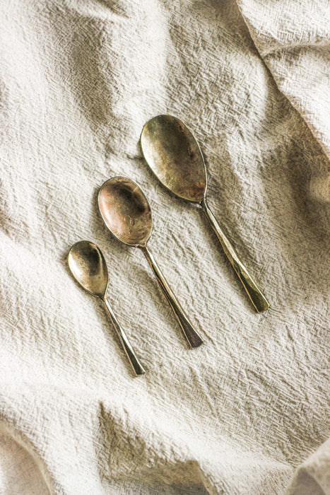 Three brass spoons on a beige linen fabric surface