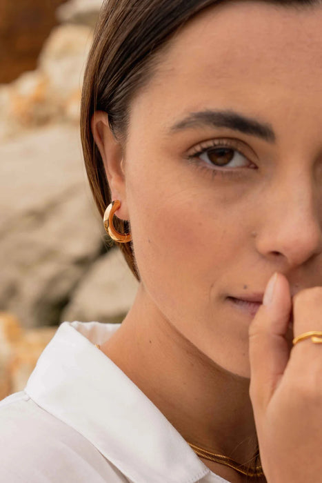 Close up of a persons face wearing gold hoop earrings and gold rings