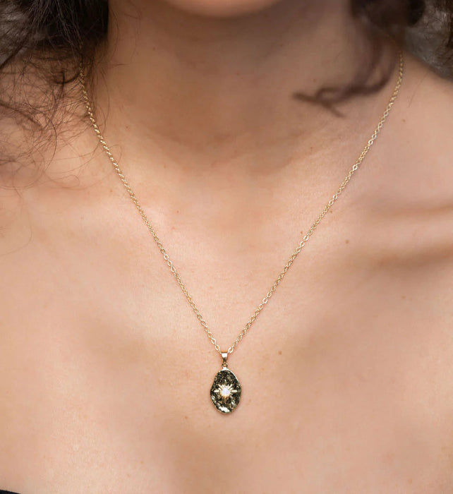 Close up of a person wearing a gold necklace with an opal stone, and gold hoop earrings 