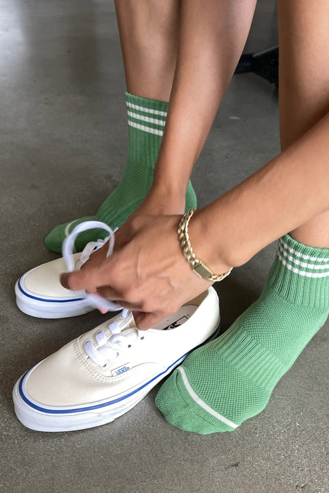 person wearing green striped socks and putting on cream trainers 