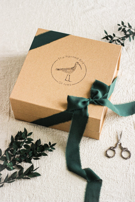 Brown gift box with green ribbon and decorative eucalyptus and sewing scissors on a beige linen surface