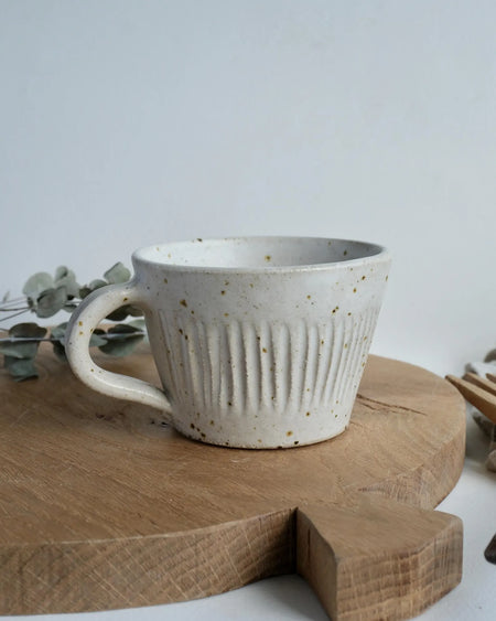 White ceramic mug with speckled texture on a wooden chopping board