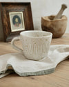 white peckled ceramic mug on a linen tea towel with a wooden frame and a wooden pestle and mortar bowl in the background