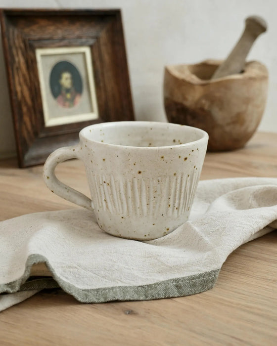 white peckled ceramic mug on a linen tea towel with a wooden frame and a wooden pestle and mortar bowl in the background