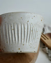 White spckled ceramic cup with textured design on a wooden surface
