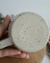 Close-up of the base of a textured ceramic mug held by a hand on a wooden and neutral background
