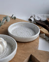 Two ceramic garlic graters on a wooden board with a white background