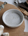 White ceramic garlic grater with textured surface on a wooden chopping board