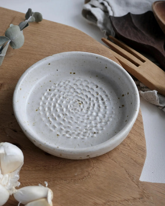 White ceramic garlic grater with textured surface on a wooden chopping board