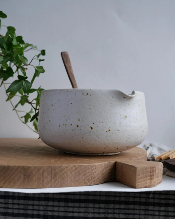 Speckled ceramic matcha bowl with wooden spoon on a wooden cutting board, plant in background
