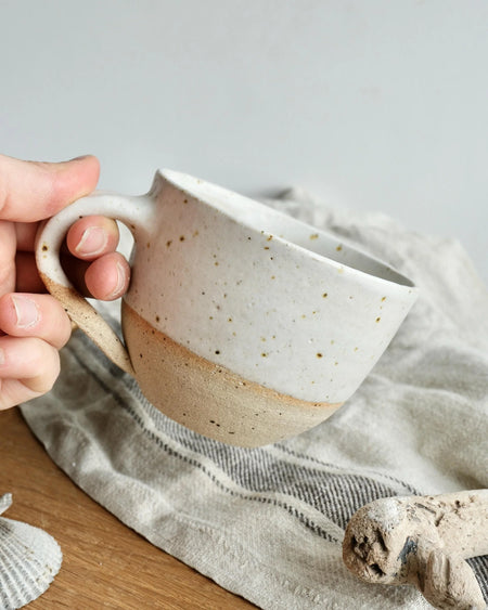 Hand holding a ceramic mug with speckled glaze on a textured surface