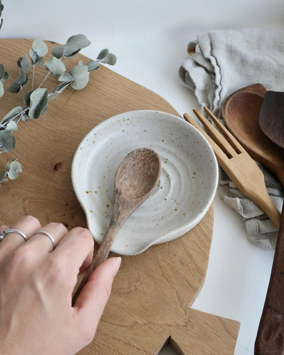 Person holding a wooden spoon over a ceramic spoon rest on a wooden board with a white background