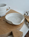 White ceramic spoon rest and mug on a wooden cutting board with a white background