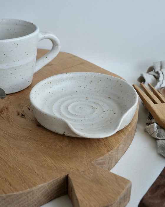 White ceramic spoon rest and mug on a wooden cutting board with a white background