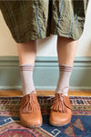 Person wearing tartan skirt, taupe socks with pink stripes, and brown loafers on a patterned rug.