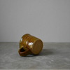 Small brown ceramic cup laying on its side on a grey surface with a plain white background