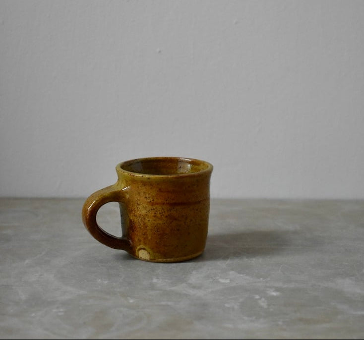 Brown ceramic mug on a grey surface with a plain white background
