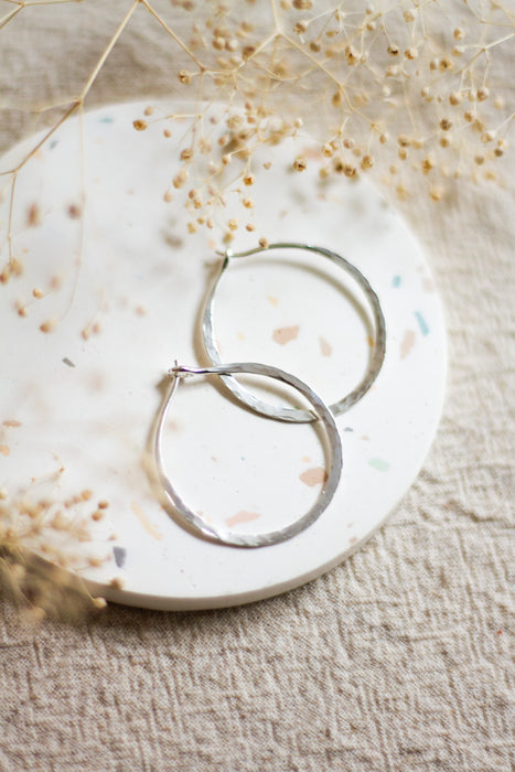 Silver hoop earrings on a textured surface with dried flowers
