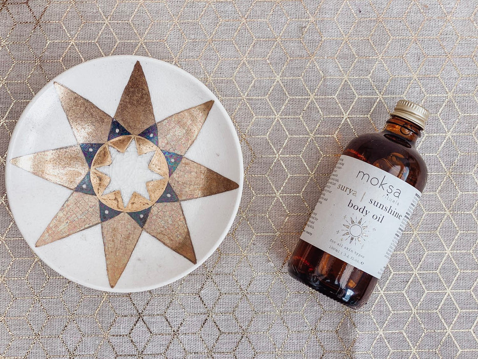 Bottle of moksa sunshine body oil on a fabric surface with a coaster