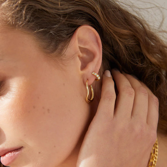 Close up of a persons ear wearing gold hoop earrings and gold rings 

