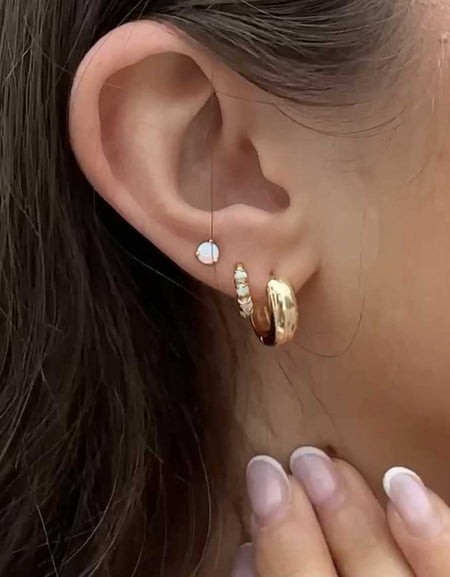 Close-up of an ear with gold hoop earrings and a hand touching the ear.