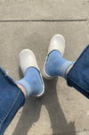 person wearing blue socks with grey clogs and jeans on a concrete pavement