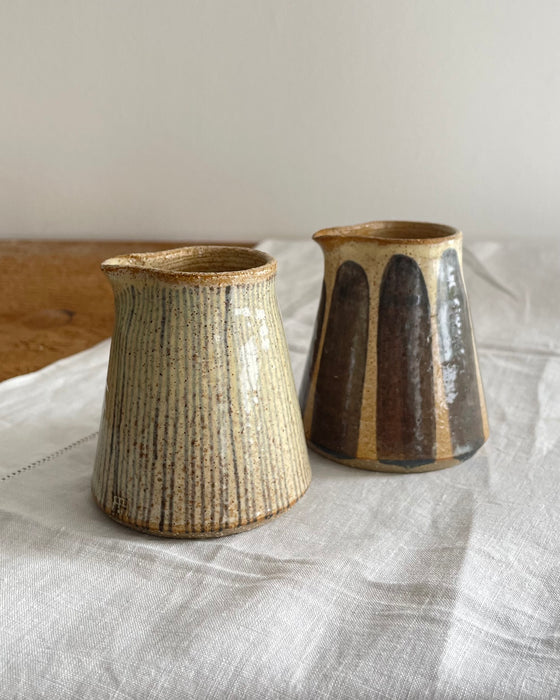 Two stoneware milk jug and matching mug in a beige glaze with a blue striped design, on a wooden table with a white cotton runner 