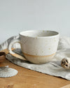 Speckled ceramic mug on a wooden surface with a light gray background