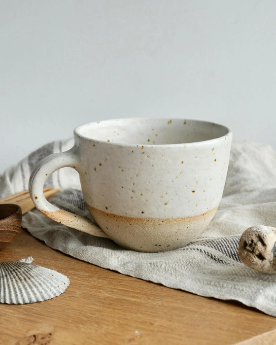 Speckled ceramic mug on a wooden surface with a light gray background