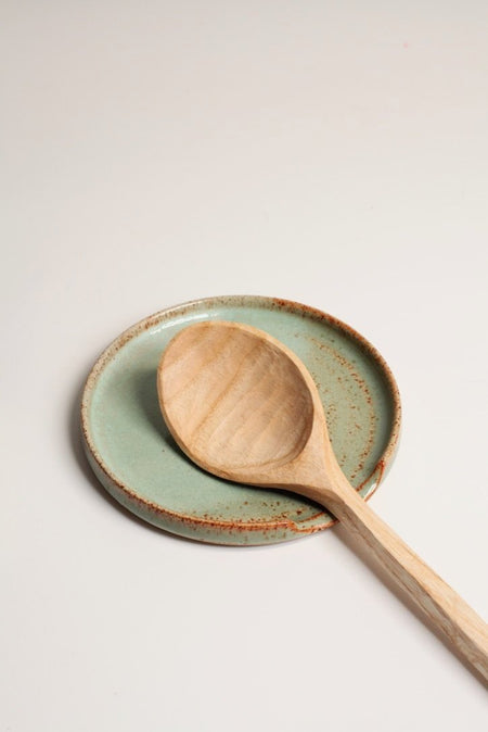 A ceramic spoon rest with a satin green glaze, displayed with a wooden spoon resting on top.